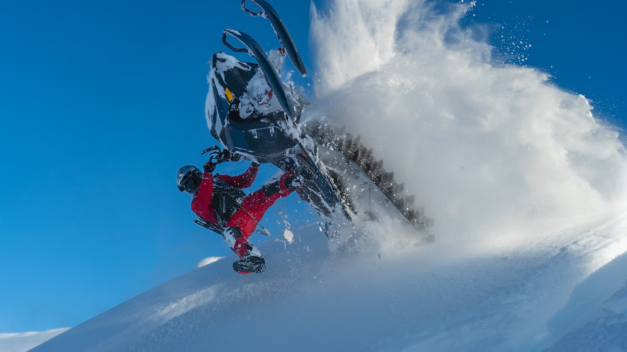 Snowmobiler launching off a cornice in deep powder under a blue sky